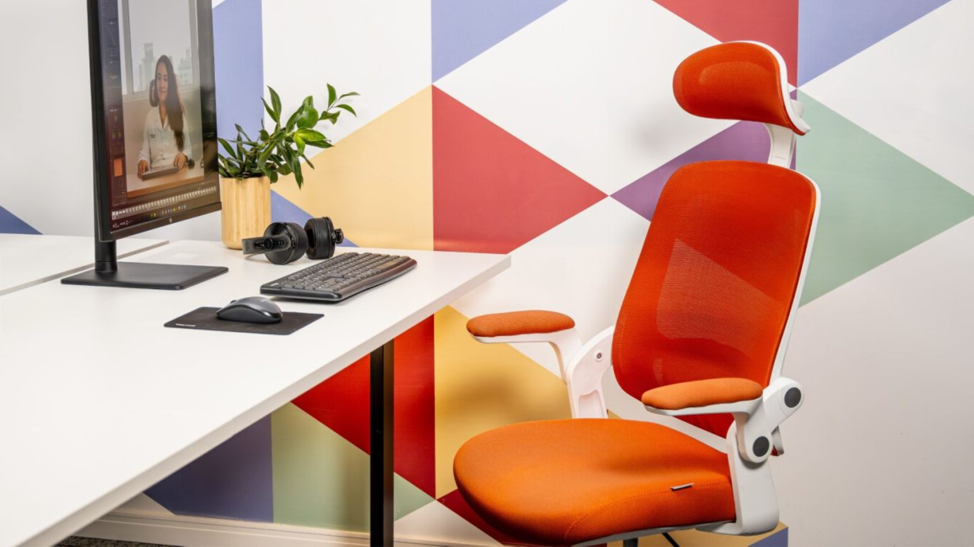 Cadeira ergonômica Astra laranja em um escritório com parede colorida.