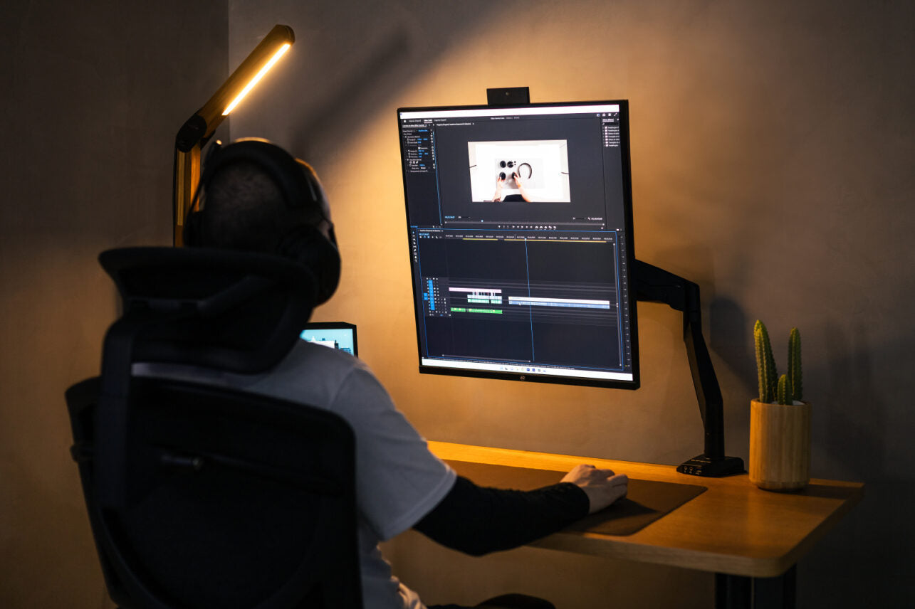 Homem em um setup completo, com mesa elétrica, monitor profissional, headset, cadeira ergonômica.