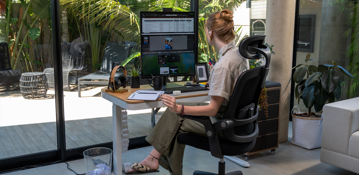 Mesa elétrica da cor branca e cadeira ergonômica preta com uma pessoa utilizando